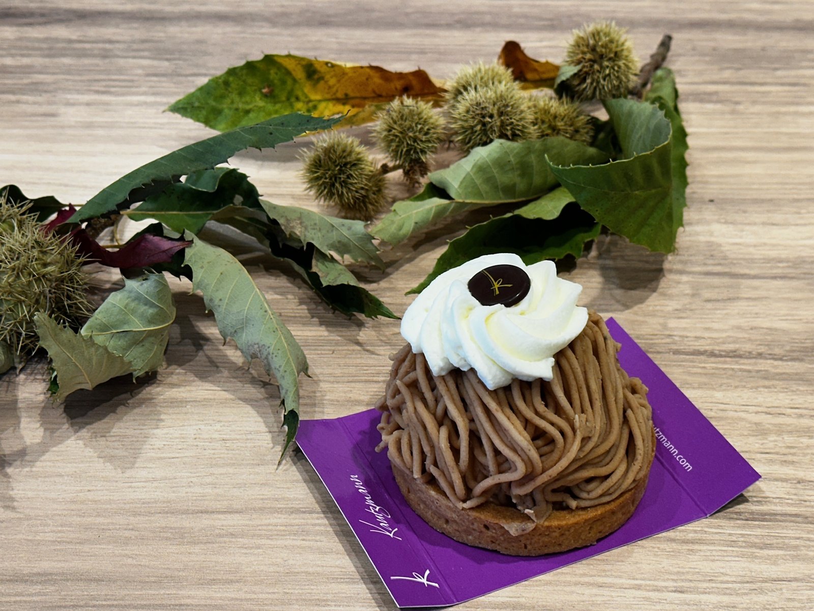 Torche aux marrons de la Pâtisserie Kautzmann sur un carton violet, entourée de feuilles et de bogues de châtaignier