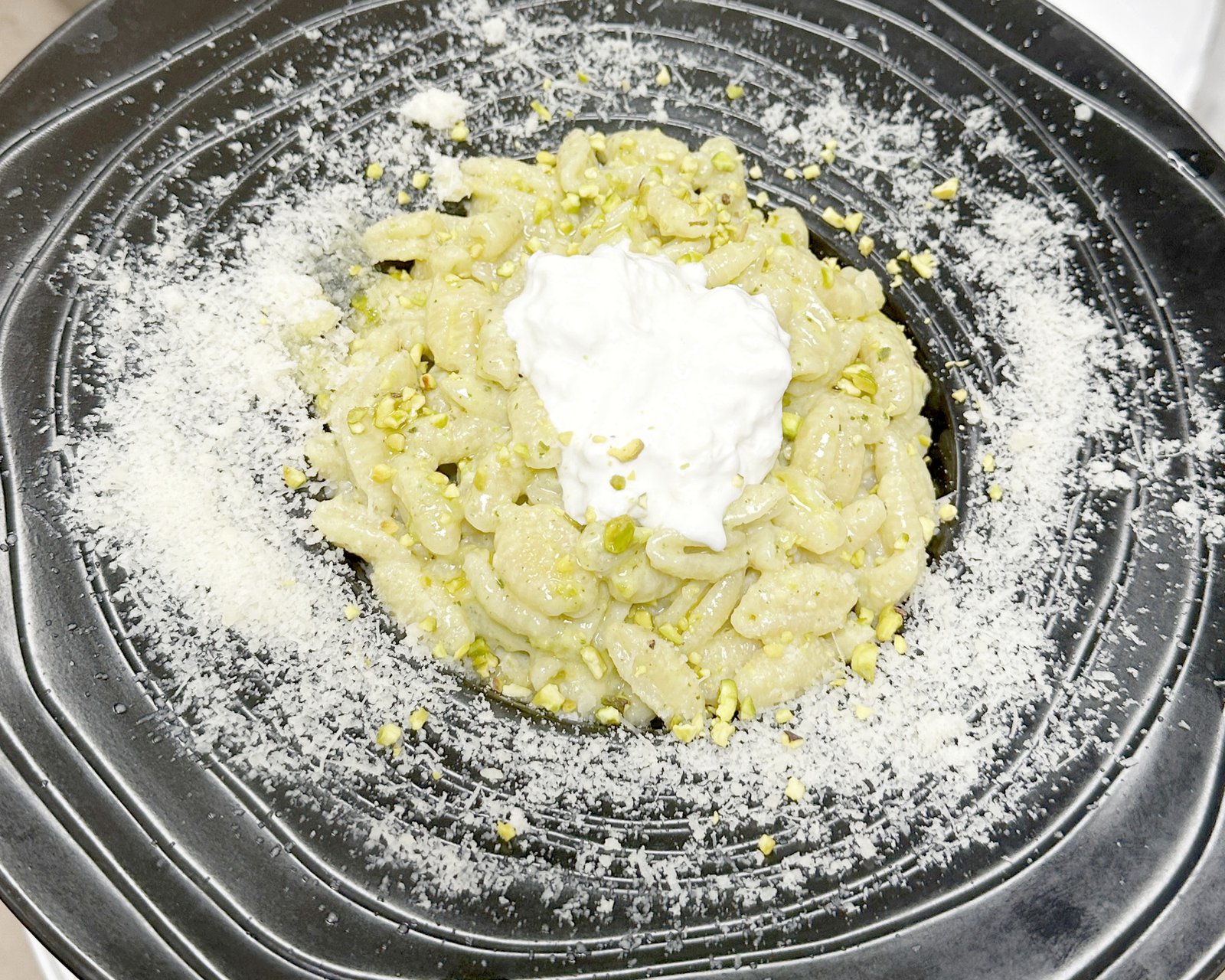 Gnocchis au pesto de pistache, cœur de stracciatella et parmesan, servis dans une assiette noire